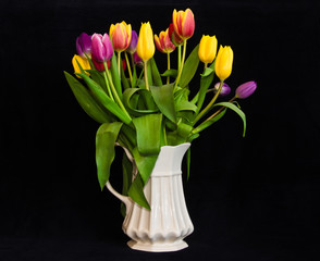 A still life with a bouquet of colourful tulips in a white vase in front of black background