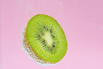 Beautiful half cut kiwi fruit floating in the soda water on pink background. High value commercial...