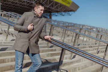 A young adult man in a gray coat walks along a city street on a sunny day in spring