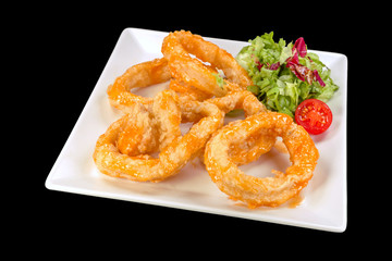 Tasty fried squid served with cherry tomatoes and lettuce on a plate, isolated on black background.