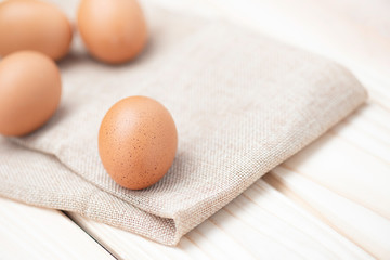 Brown chicken eggs on burlap cloth and on wood table and front egg in soft focus.