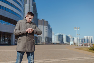 A young adult man in a gray coat walks along a city street on a sunny day in spring
