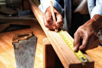 Closeup of a woodworker in his workshop marking a board for cutting.