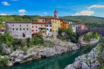 Fototapeta na wymiar Kanal ob Soči in Slovenia. Picture of beautiful colorful buldings standing on a stone with Soča river and bridge. 