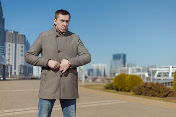 A young adult man in a gray coat walks along a city street on a sunny day in spring
