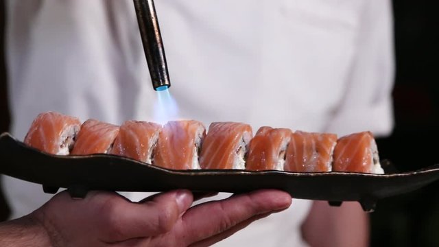 Professional sushi chef preparing roll via fire from gas burner