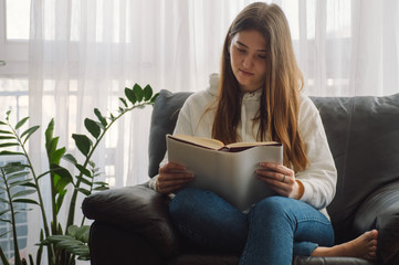Reading and development. Beauty young woman is reading a book at home. Thoughtful girl reading...