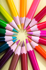 Naklejka premium Colored pencils arranged in a circle, macro photographed from above on a yellow background.