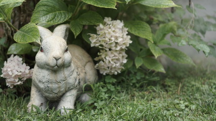 Stone rabbit hide in a bouquet of white viburnum in the garden / forest. Smoke / foggy atmosphere in the outdoor.