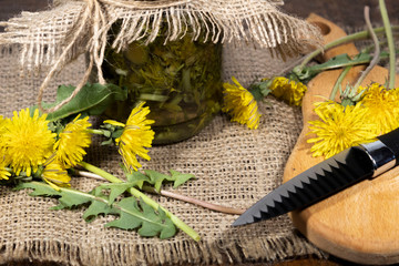 On the table in the bank is a tincture of dandelions. On a cutting board are dandelion flowers and a knife.