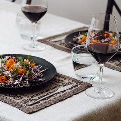 Photo of a home cozy supper with glass of red wine and salad from fresh eco vegetables on black plate indoors