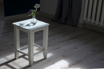 white old stool is in the middle of the room with a vase with flowers of burdock. Horizontal frame.