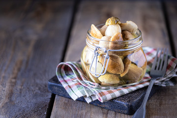 Mushrooms in a glass jar. Homemade fermented porcini mushrooms on a wooden dark background. One mushroom on a fork. Copy space.
