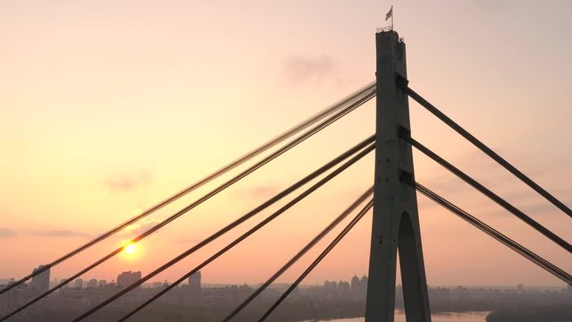 Aerial drone view View Of North or Moscow Bridge Kiev, Ukraine over Dnieper. Drone span between the cables of the bridge. Sunset sun. City view. Rays of the sun through the cables of the bridge
