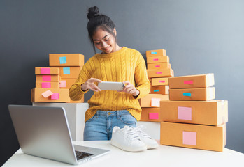 Young women taking photo to shoes with cell telephone or smartphone digital camera for post to sell online on the Internet and preparing pack product box. Selling online ideas concept