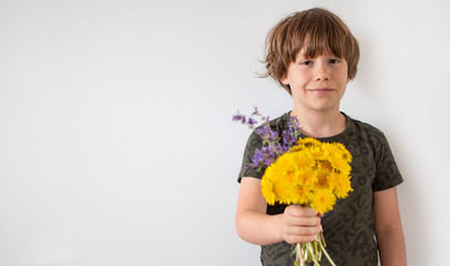 Uśmiechnięty chłopiec trzymający bukiet polnych kwiatów, białe tło. © tzalinechka