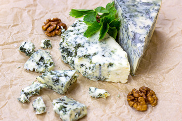 Slices and triangles of Danish Blue (dorblue) cheese with mold on a light paper background.