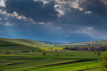 Storm clouds over beautiful green meadow at springtime, visible small hungarian Transylvanian village.