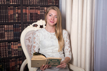 young pretty woman in white clothes holds retro book sitting in old fashioned chair