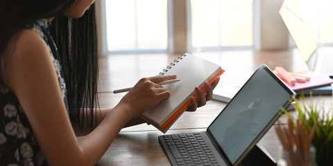 Cropped of young entrepreneur woman taking notes while sitting in front her computer tablet with...