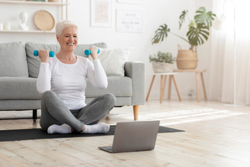 Active senior woman in sportswear exercising with dumbbells, practicing fitness at home, empty space