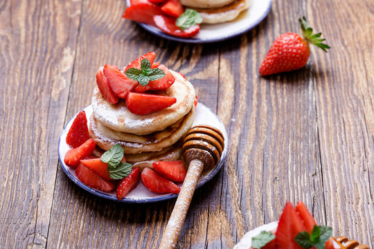 Pancakes with fresh strawberries on wooden table