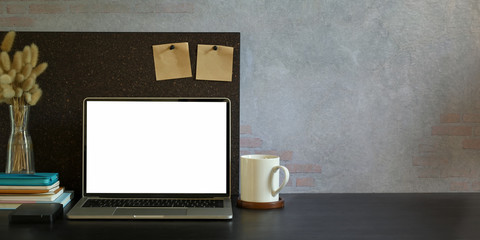 Computer laptop with white blank screen putting on black working desk and surrounded by coffee cup,...