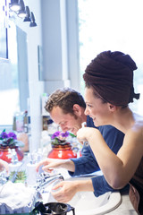 coppia di giovani fidanzati si prepara in bagno sorridendo: lei si lava i denti con lo spazzolino elettrico e lui si lava la faccia