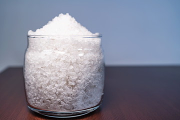 white crystalline salt in a transparent glass jar scattered on a brown table