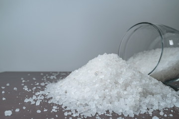 white crystalline salt in a transparent glass jar scattered on a brown table