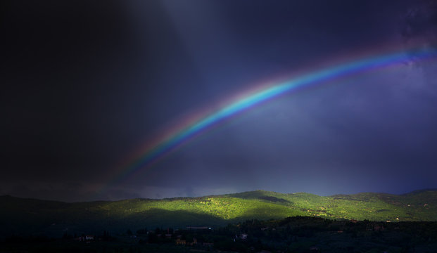 Rainbow in dramatic dark sky over green hillside;  beautiful summer countryside landscape