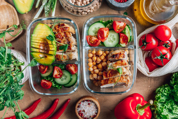 Healthy meal prep containers with chickpeas, chicken, tomatoes, cucumbers and avocados. Healthy...