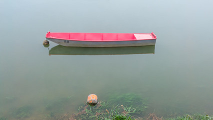 Fishing boat moored along the riverbank in deep fog. Autumn gloomy foggy scene of vessel and river wrapped in a veil of mist.