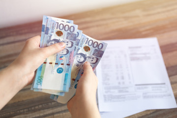 Hands holding cash banknote of one thousand Philippines peso paying bills, payment or salary.  White background, close up