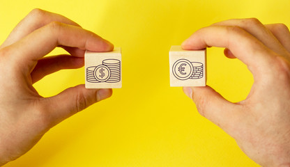 Hands holding cubes with dollar and euro icon on yellow background.
