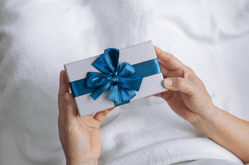 Elderly women hands holding gift box with blue ribbon and Sleep on the bed with a white blanket