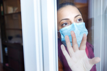 Fototapeta na wymiar ragazza con la mascherina chirurgica guarda fuori dalla finestra attraverso un vetro con aria triste