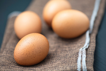 Brown chicken eggs on dark brown burlap cloth and on black wood table and front egg in soft focus and thin depth of field.