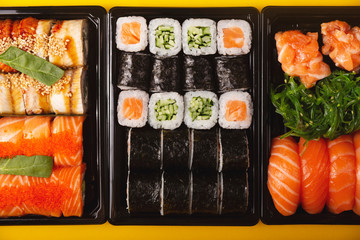 Sushi with fresh fish salmon and eel delivery in containers to the house on a bright yellow background. Top view, flat lay.