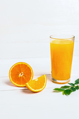 Orange juice in a tall glass. Cool drink on a white wooden background. Sliced ​​orange and green twig with leaves. Empty space for text.