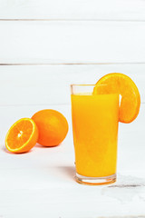 Orange juice in a tall glass. Cool drink on a white wooden background. Sliced ​​orange in the background. Empty space for text.
