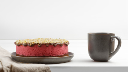 Homemade raspberry cheesecake sprinkled with walnuts crumbs and cup of tea on white wooden table. Front view.