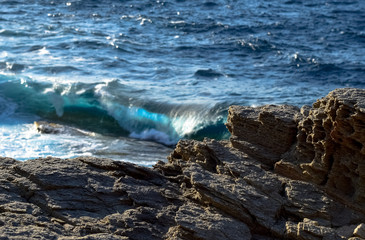 Cliffs at the Aegean sea in Ikaria with blue waves breaking on the shore, Greece