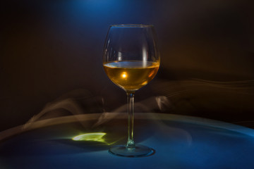White wine in a glass on the table on a creative black background. Cigarette smoke in the bar and an alcoholic drink at a party or disco. Shooting in the dark key. Copy space.
