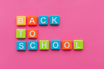 Back to school concept. Phrase "Back to School" from alphabet magnets on pink background. Top view. Copy space