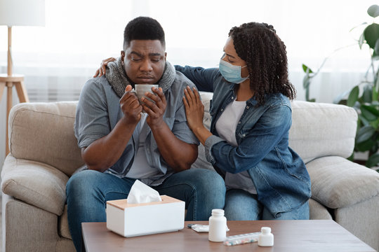 Loving Woman In Medical Mask Caring About Sick Husband At Home