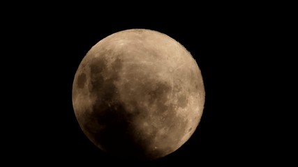 A pink full moon rising from behind dark stormy clouds against a pitch-black night sky. Viewed on the 07/04/20 from South Africa.
