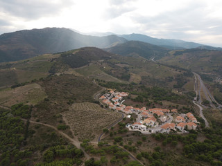 Aerial view from drone. A small town in the mountains, surrounded by fields and winding serpentine roads. The orange roofs of the village houses between the mountains are illuminated by the sun.