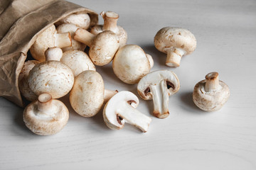 Mushrooms champignons in paper bag on a white wooden table. Place for text or advertising. Top view