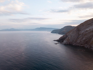 Fototapeta na wymiar Aerial top view shot from drone. The speed boat rushes over the horizon on the vast Mediterranean sea among the majestic stone mountains and blue haze covering the sky. France, Port-Vendres.